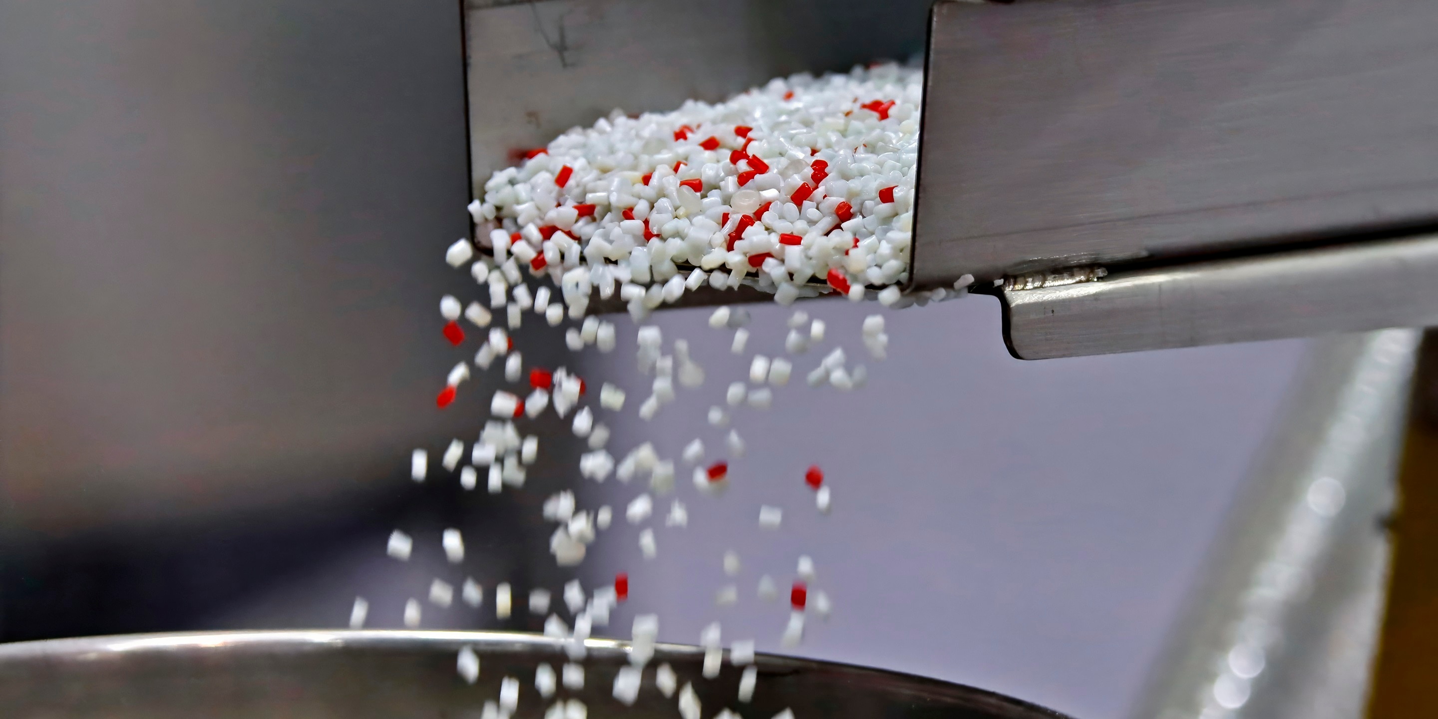 Recycled plastic resin granules being processed through an industrial hopper for injection molding production